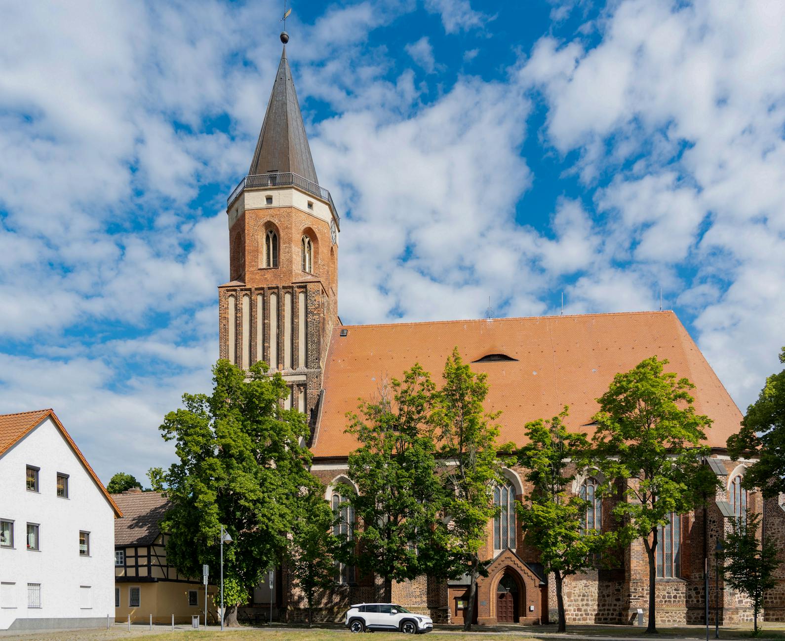 Gotycki kościół z wysoką wieżą na tle błękitnego nieba i drzew