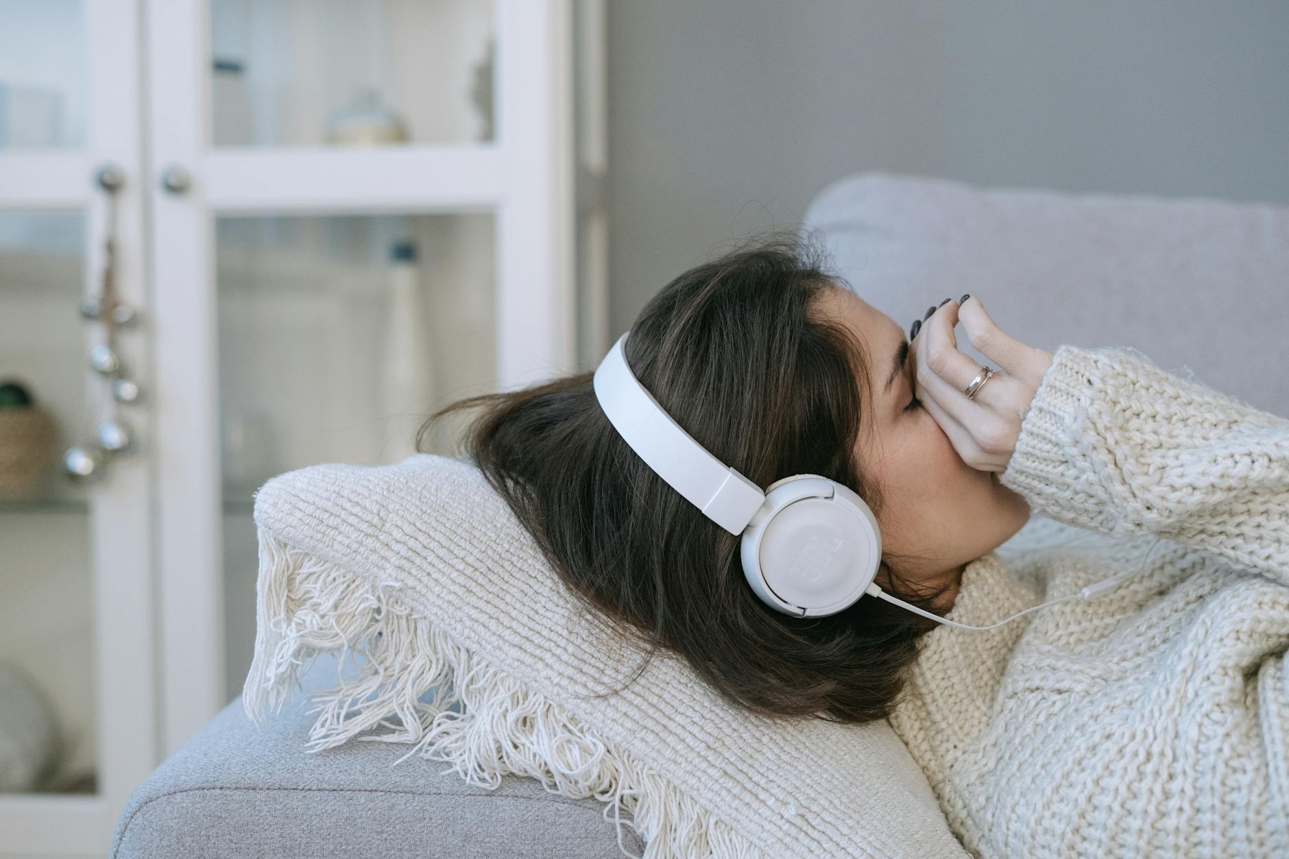 Dlaczego muzyka smutna potrafi poprawić humor? Kobieta na kanapie ze słuchawkami, zadumana przy muzyce