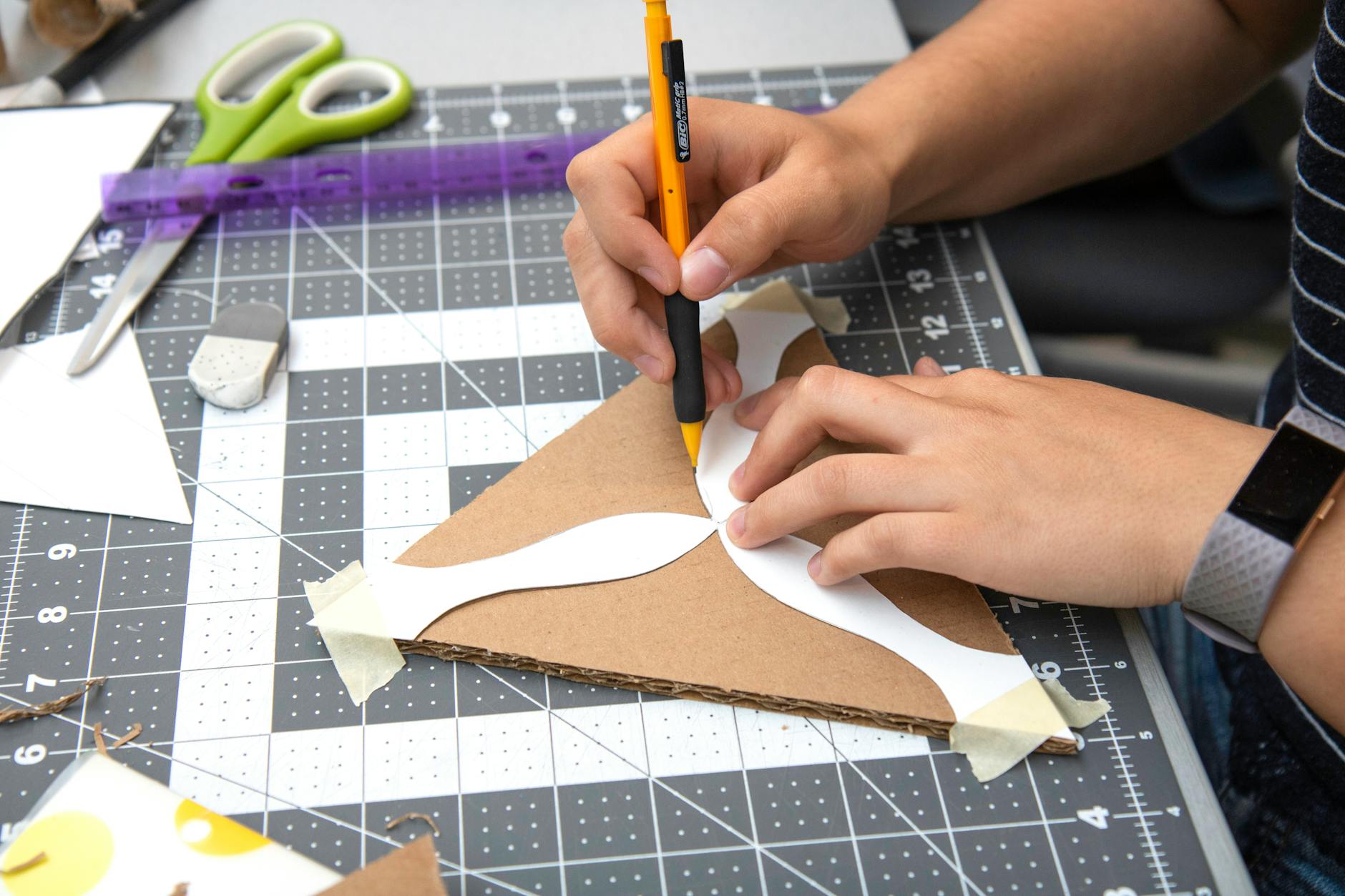 Osoba mierząca linijką karton na macie, ołówek i narzędzia obok