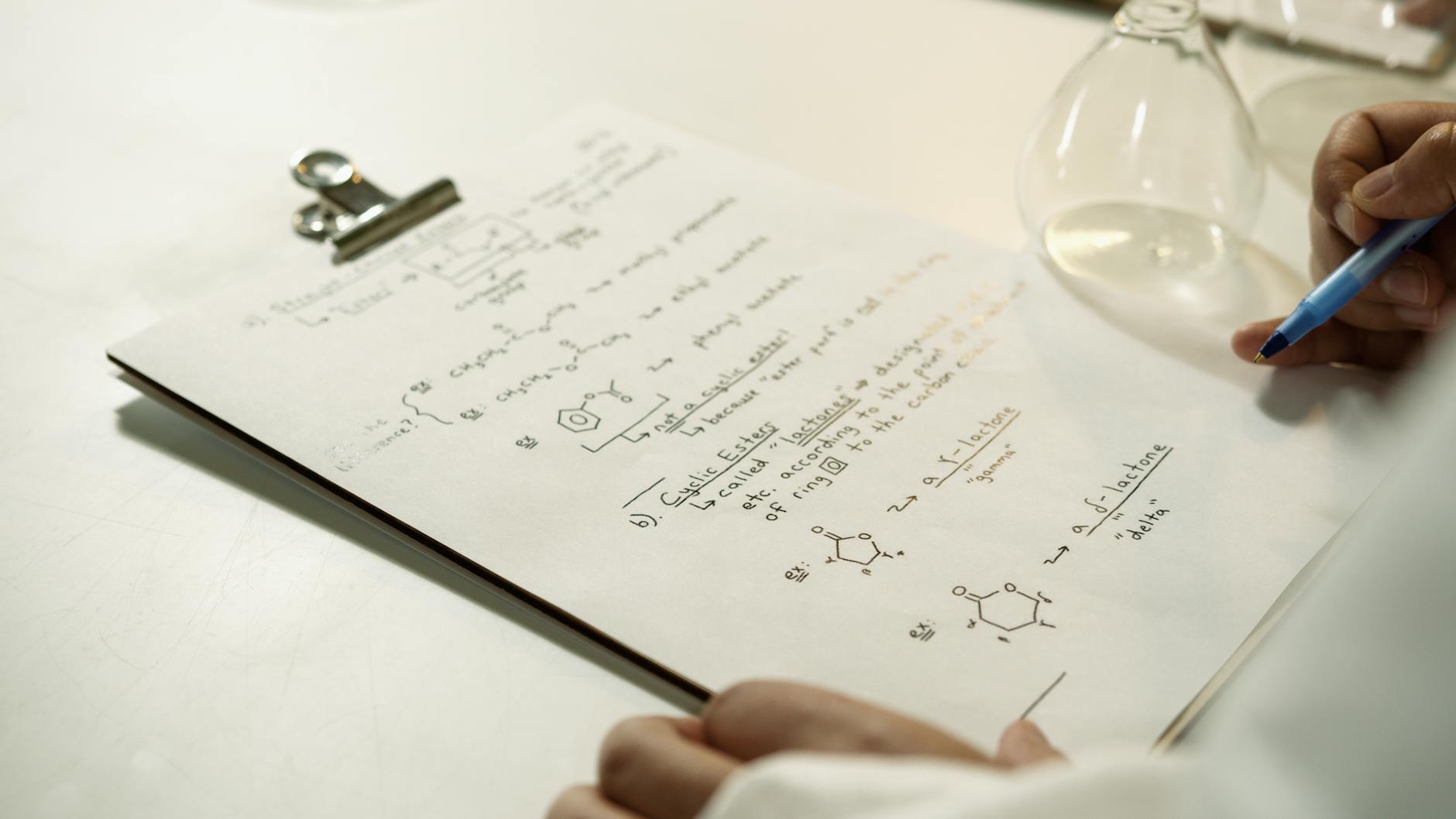 Zbliżenie na ręcznie zapisane wzory chemiczne na clipboardzie w laboratorium