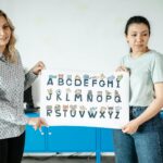 Dwójka nauczycieli trzyma plakat z alfabetem w szkolnej klasie