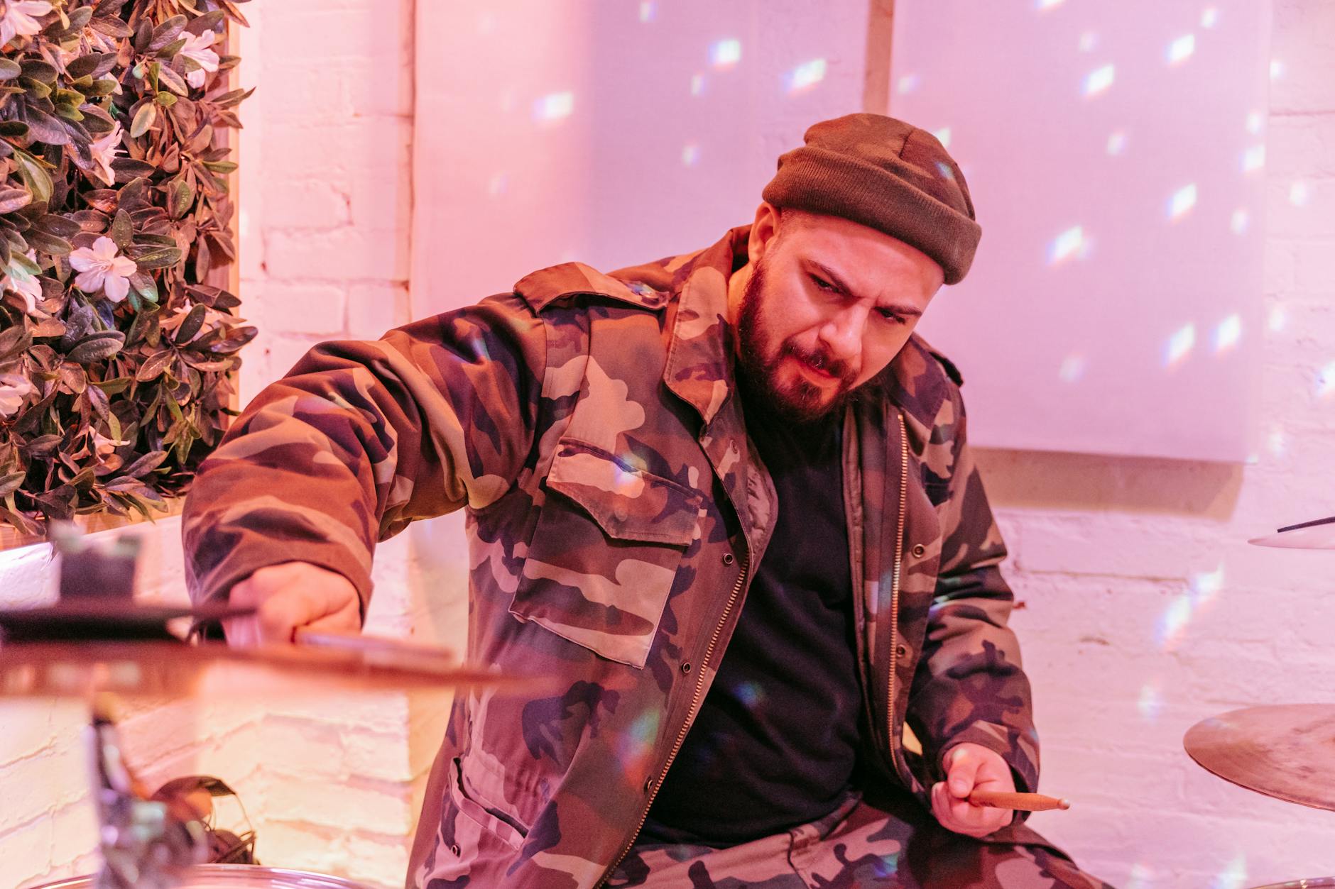 Perkusista w wojskowej kurtce gra w różowym, nastrojowym pomieszczeniu