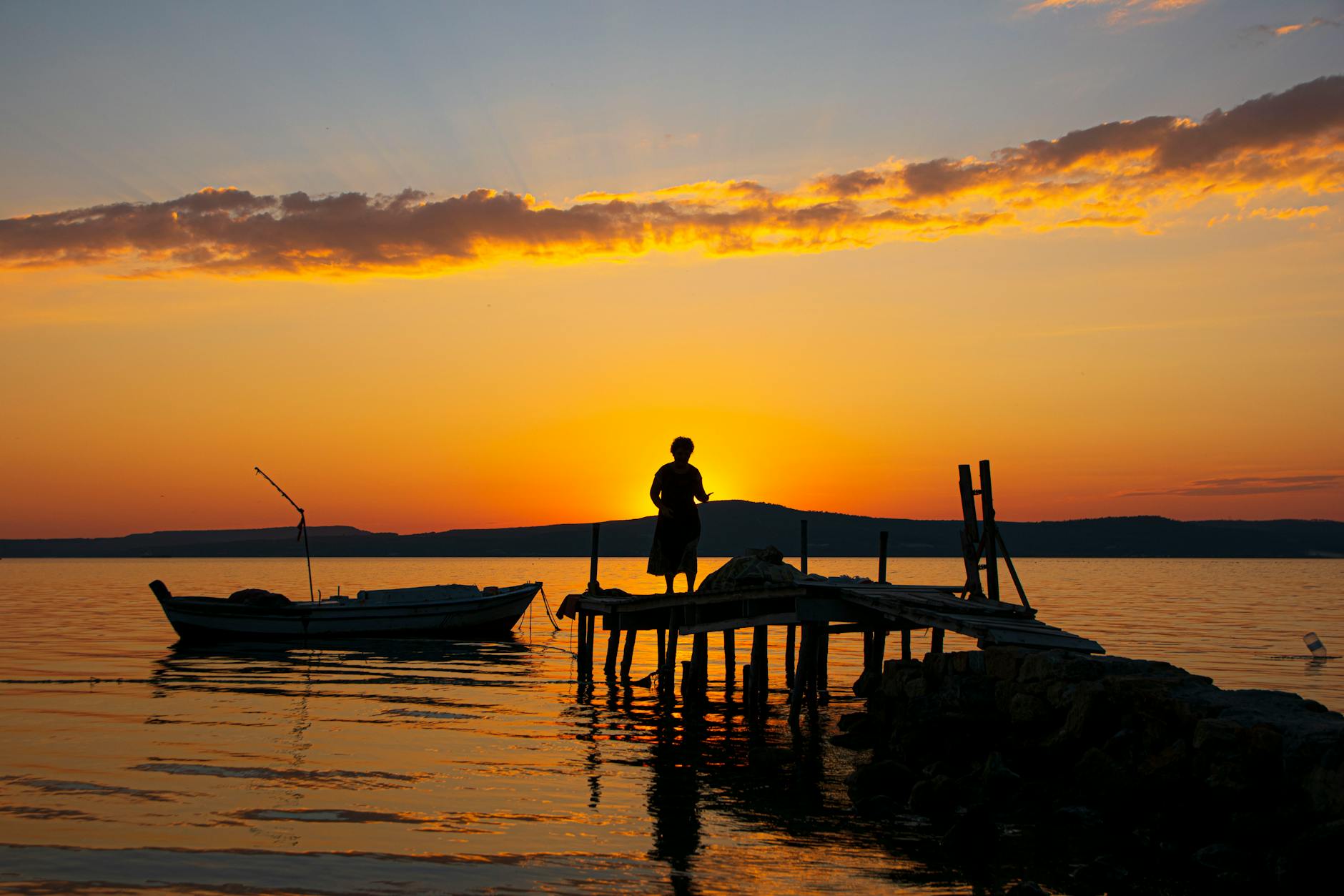 Sylwetka osoby na pomoście o zachodzie słońca nad spokojnym jeziorem