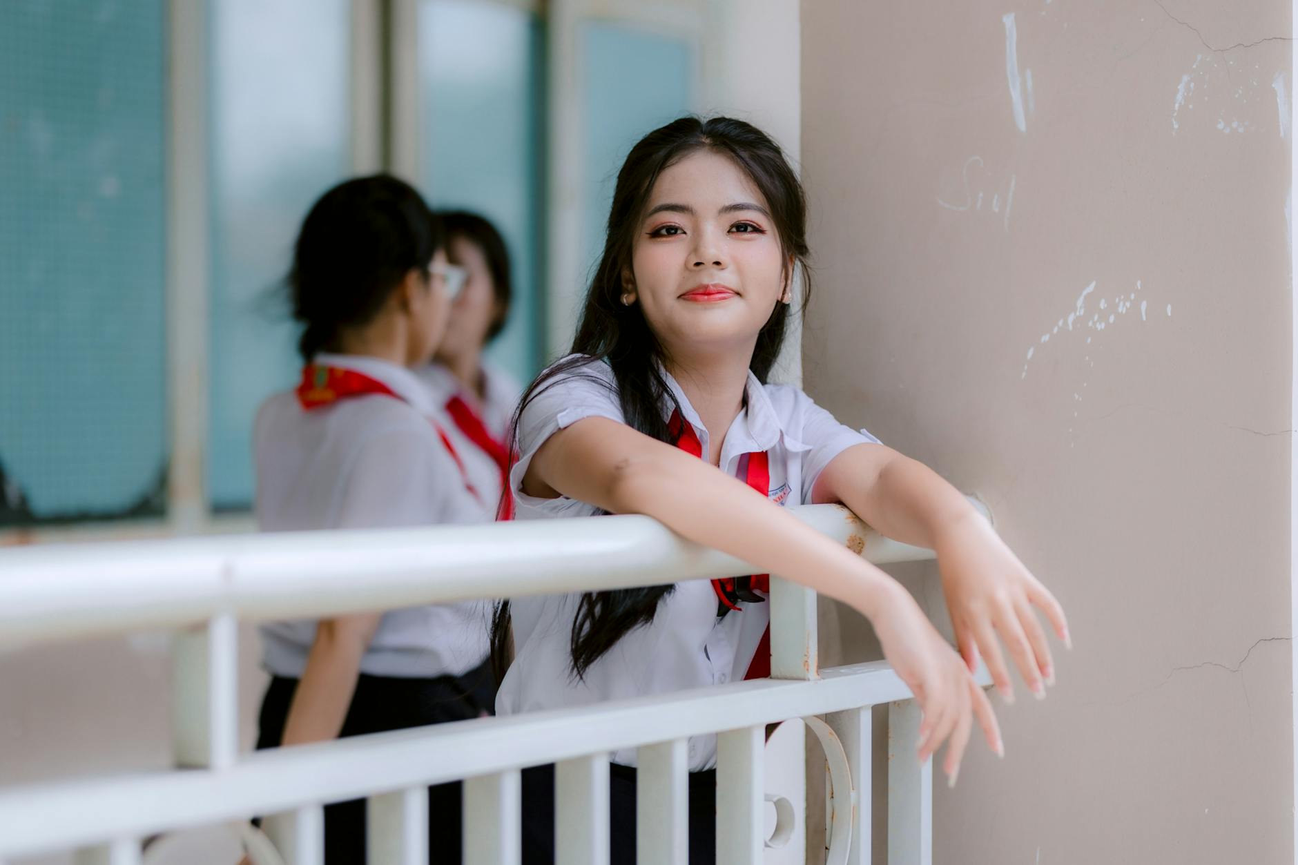 Uśmiechnięty azjatycki uczeń w mundurku szkolnym oparty o barierkę na dworze