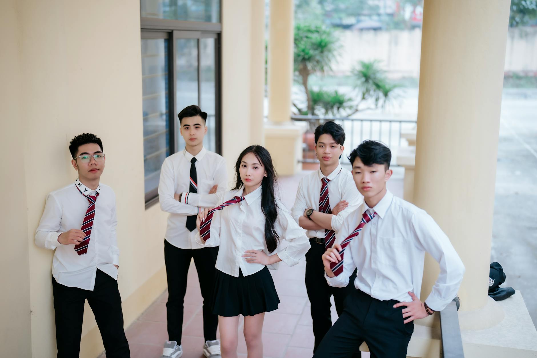 Uśmiechnięci nastolatkowie w szkolnych mundurkach przed budynkiem szkoły