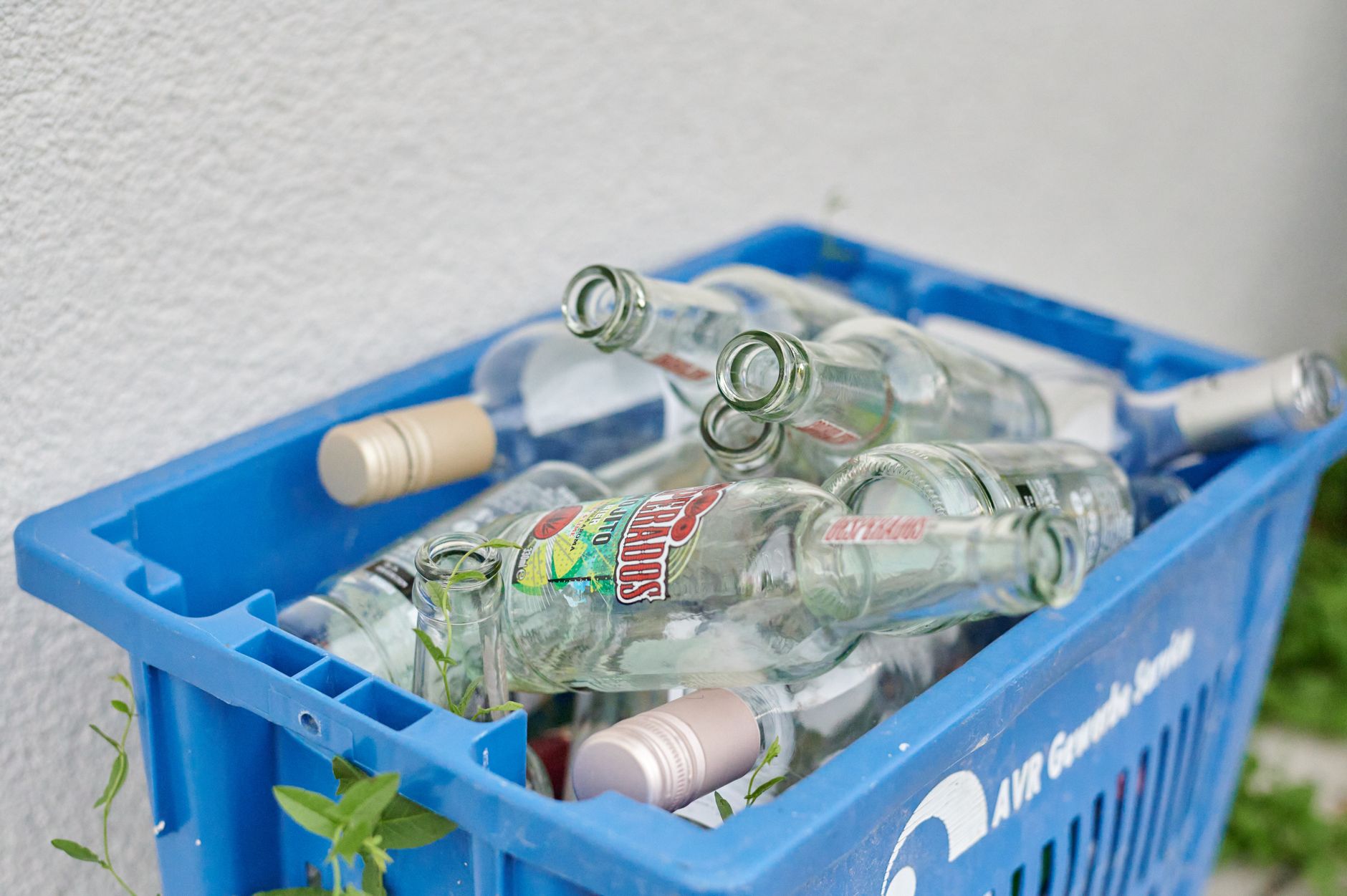 Recykling szkła: dlaczego nie każda butelka nadaje się do przetopu? Niebieska skrzynka z pustymi szklanymi butelkami do recyklingu